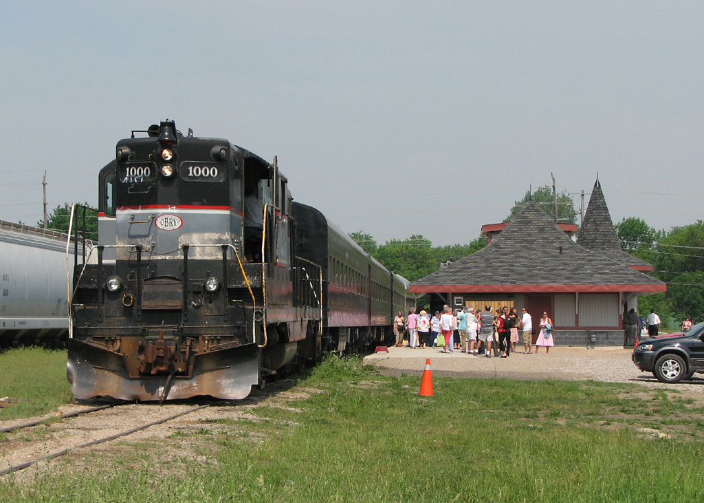 With passengers lingering around the platform of the new station, OBRY\'s 1000 waits to depart with the Credit Valley Explorer on a sunny morning in Orangeville.