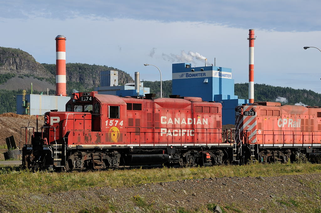 Since sidelined at the shops in Thunder Bay, CP GP9u 1574 works with sister 1629 interchanging CN revenue for empties in the \"West Yard\" as they work the afternoon Bowater job. In late 2009 CP went from 3 shifts a day to 2 and Abitibi-Bowater has thrown a chain link fence ultimately ruining this photo angle.