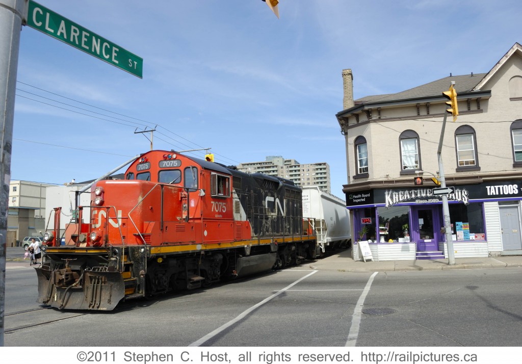 Tattoo You: CN 7075 has entered Clarence St and is running against the flow of street traffic, protected by a traffic light interlocking mechanism which was actuated earlier by the Conductor. This wide angle view shows the intersection of Clarence St and Colborne St.
