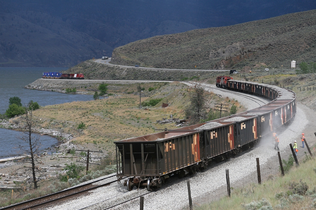Work 5952 dumps ballast on the new track at Savona while Olympic GEVO 8866 skirts the shores of Kamloops Lake