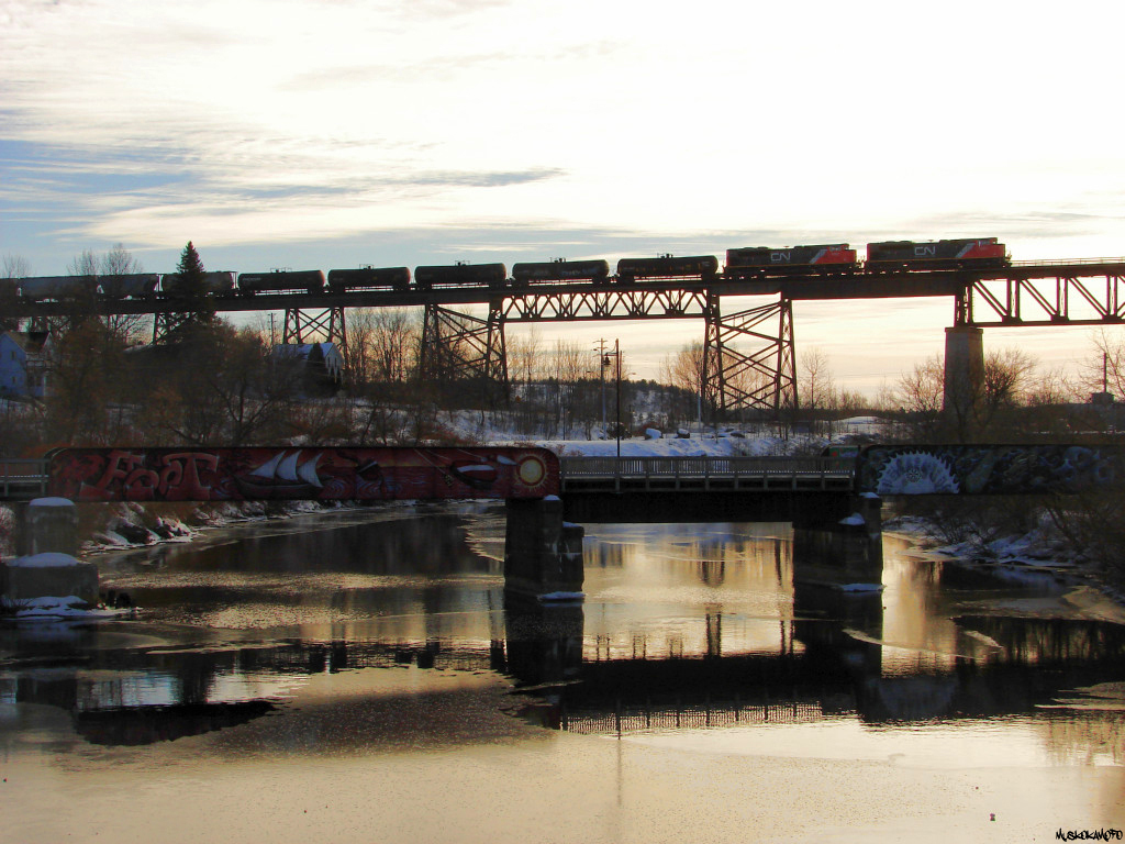 CN 301, with brand new CN 8884/8880 fly through the air over the town of Parry Sound in the setting winter sun, the bridge in the foreground was part of the former Ottawa, Arnprior and Parry Sound Railway line onto the reserve down to Depot Harbour, interchanging with CN at South Parry, taken over by CN in 1959 and abandoned shortly after, has been reduced to a walking/snowmobile trail.