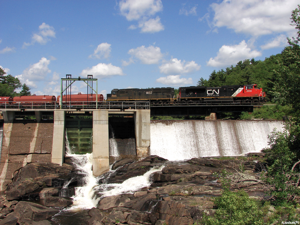 CN X316 pulls across the Seguin river in Parry Sound as clouds break up overhead, this extra from Winnipeg had CN 8856/IC 1032 pulling 85 cars.