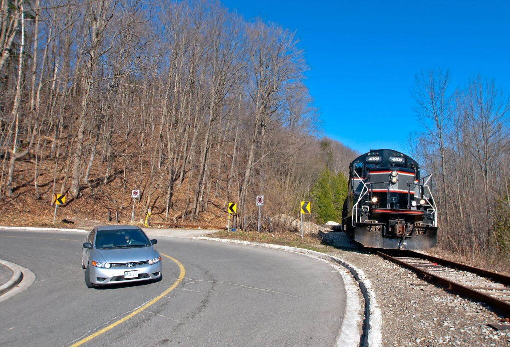 A locomotive and a car meet at a sharp hairpin curve in the road, both technological wonders from different frames in time, both built in Canada, the Japanese designed Civic built in Alliston, Ontario and the American designed ex CN GP9RM built in London, Ontario. With 5 cars to interchange to the CPR at Streetsville, the southbound twice a week train from Orangeville is seen here passing Forks of the Credit.