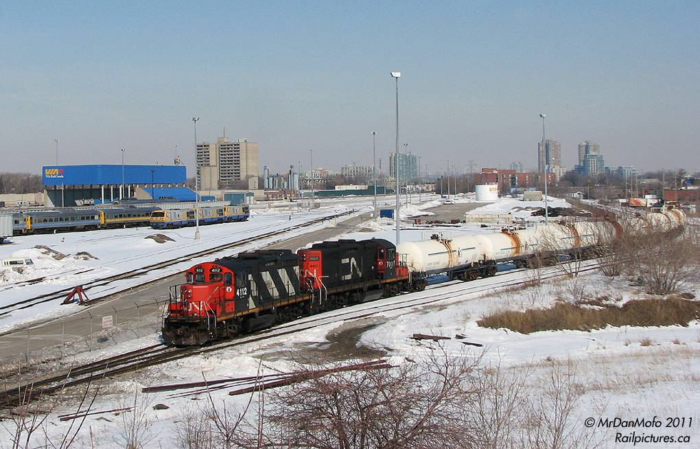 In a rarely-caught move, CN local 543 with GP9RM\\\'s 4112 and 7007 takes the industrial lead tracks to CN\\\'s Mimico Yard, heading past the wye and south end of VIA\\\'s Toronto Maintenance Centre. Retired LRC\'s, RDC\'s and stored garbage gondolas little the yard, and past the VIA fueling building is the CN Oakville Sub\'s mainline trackage.