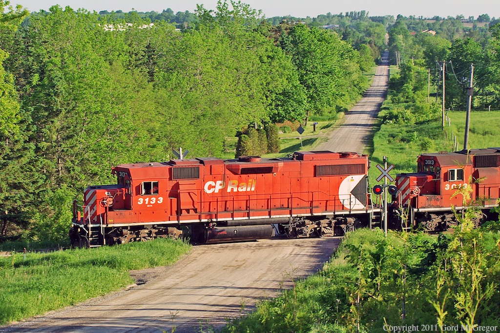 3113 Leads T07 through the beautiful countryside west of Norwood behind it is a rare visitor from western Canada 3013 a GMDGP-38AC.