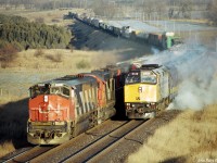 A westbound VIA train has just come to a stop in a cloud of steam after being nailed by the hotbox detector at Newtonville in March 1986.  CN 393, led by HR-616 2105 and two six-axle MLWs passes the VIA train's head-end.