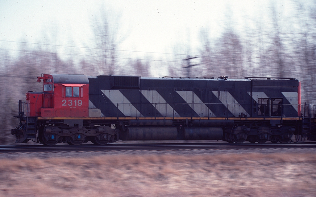 Panned shot of CN M-636 2319 leading an eastbound at track speed near Colborne, ON on the Kingston sub in March 1990