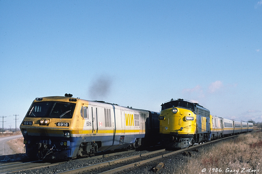 FP9 6510 has coupled onto to a disabled train 41 and completed the brake test and is not yet on the move as train 53 passes it at Parkway Road, Darlington Park, just east of Oshawa on Dec 13th, 1986. Photo by Gary Zuters, scan by John Reay with permission.