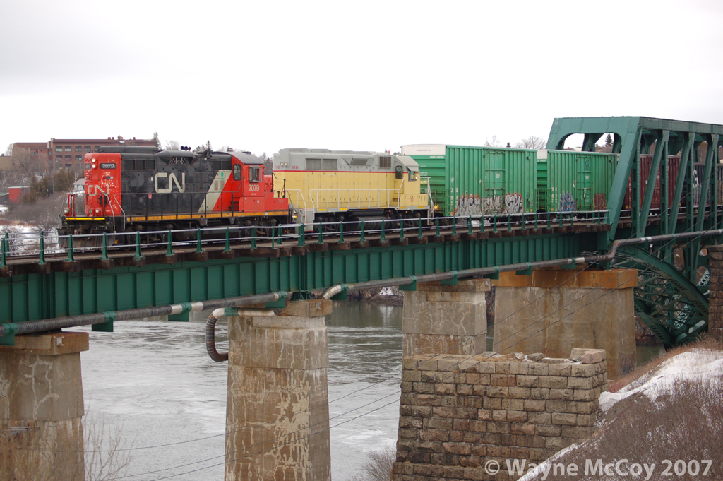 Leased shiny CN7079 and new-to-NBSR 110 cross the Reversing Falls Bridge westbound with a transfer from Island Yard.