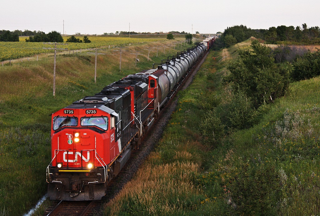 CN Q199 with repainted 5735 and 8909 head under the wooden overpass at Miniota and down hill to meet M312