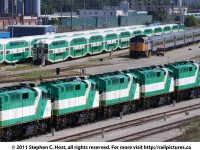 A row of stored GO F59\'s (10 in total, only 5 pictured) sit stored, numbers blanked out, reportedly sold to AMT for commuter service in Montreal and are awaiting transfer. In the background is VIA and GO equipment laying over after the morning commuter rush.