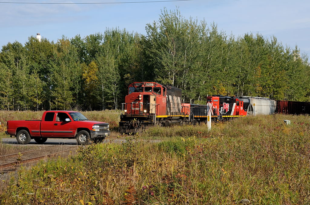 A red truck speeds infront of CN 5279-CN 238-CN 7258 as they click along the old Abitibi Mill spur located off the CN Mission Spur in Thunder Bay, ON. Pieces of the old Abitibi Mill at the end of the spur is being demolished and hauled out via rail in old wood chip gons and (regular) gondolas.
