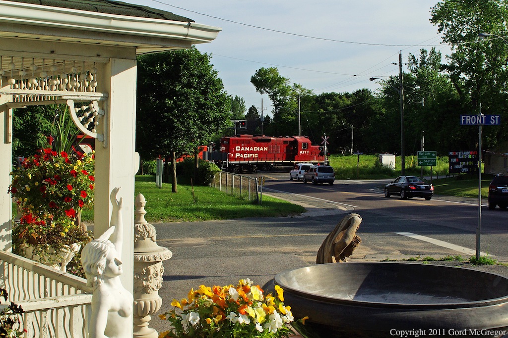 Statues and cars alike wait as 8211 a GP9 leads T07 in historic Myrtle Station on Canada Day.