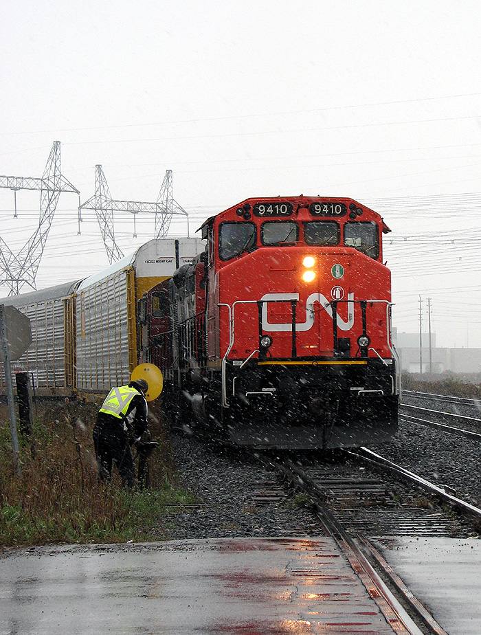 Waiting at the busy Torbram Rd crossing in the falling snow, CN 9410 with still-fresh zebra fresh paint leads 577, the CN-CP Lambton transfer run, as it waits to enter Malport Yard. After the conductor trainee is tends to the switch, 577 will proceed into Malton yard with its interchange cars from CP.