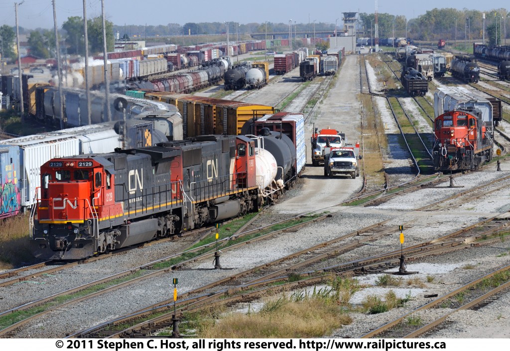 CN 2129 is leading CN 509 who is building their train @ Sarnia, with CN 393 heading to Port Huron beside it on the left. To the right is a CN remote control yard job performing switching duties in what is known as Sarnia \"A\" yard.