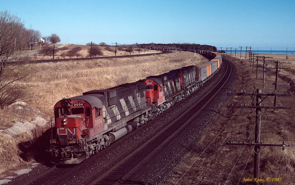 A brace of CN 6-axle MLWs on a container train approaches the Lakeshore Road bridge adjacent to CP Lovekin. The slide mount says May 1987.
