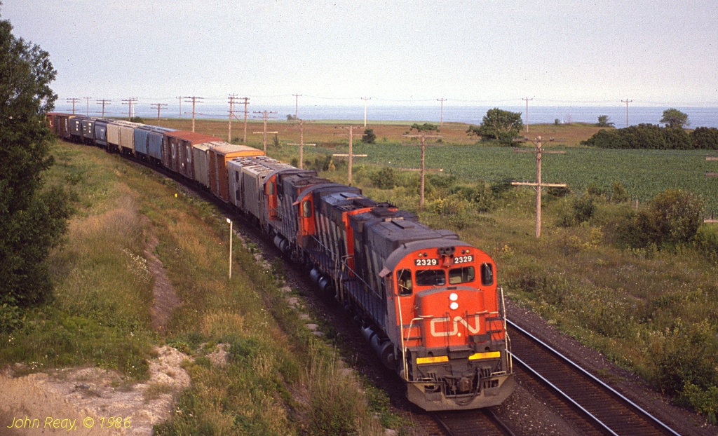 CN MLW M-636 2329 leads a wesbound at the Lakeshore Road bridge at MP 284 CN Kingston sub, late in the afternoon on a Sunday in July 1986.