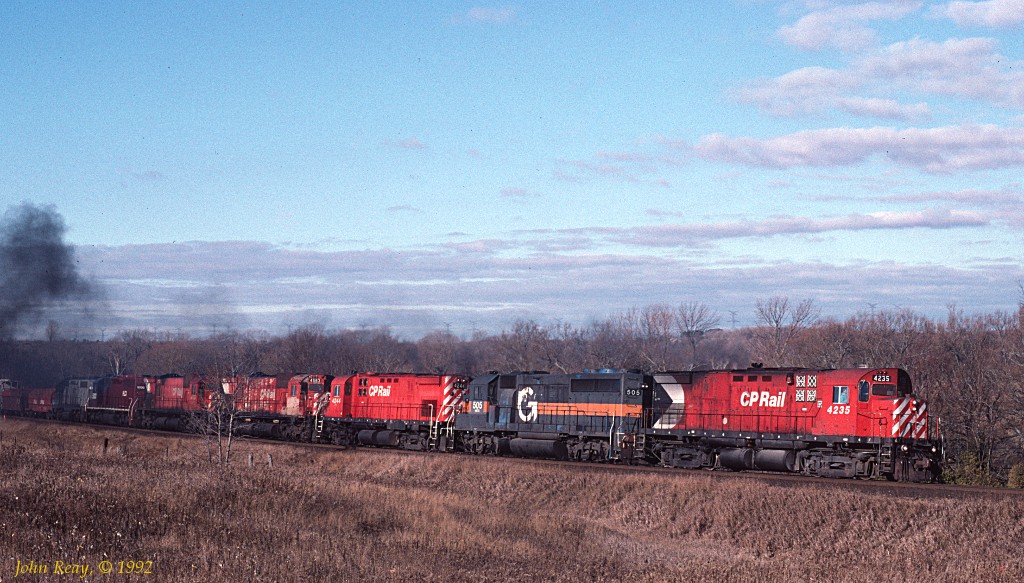 The typical Belleville sub \"zowie\" lash-up of the era consisting of two C-424s, two M-636s and three rent-a-wreck leasers, is seen near Elliott Road, Newtonville (MP 151) with the 4235 in the lead. I leave as an exercise for the viewer to determine which unit is responsible for the puff of smoke stage left.