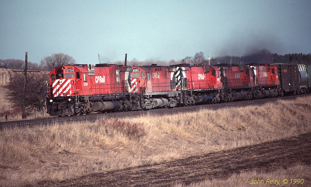 CP MLW M-636 4704 leads several sisters and cousins westbound at Lovekin siding, CP Belleville sub, in April 1990.