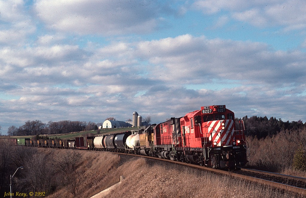 CP GP9 8207 leads a C-424 and an ex-UP leaser on an eastbound over highway 2 just east of Newcastle village.