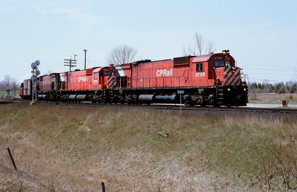 Departing Agincourt Yard May 4, 1980, CP Rail train #942 enters the high rail at Staines, Ontario with a seventies superpower trio 4729 (M636) / 4565  (M630) / 4737 (M636). The big M units had a propensity to leak – anything – witness the fresh oil stains on 4729\'s front fuel tank, 4565 is in fresh paint and shows evidence (blistered paint) of possible exhaust leak and/or turbo overheating below the exhaust stack (see also trailing image provided) and no doubt the head end crew is happy they are not occupying leak prone 4737 (see trailing image) where the cab is covered in oil thrown off the sixteen cylinder ALCO designed engine. Kodak Kodacolor II ASA100  negative transported by a Nikon Nikkormat EL. Photographer S. Danko.