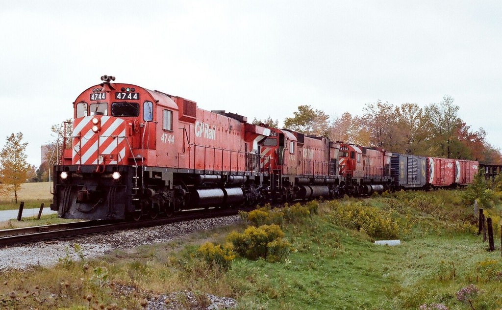 High horsepower seventies style: ten thousand six hundred rated horsepower or is this ten thousand two hundred horsepower? CP Rail first #942 approaches the high iron at Staines, Ontario (east end Agincourt Yard) powered by Diesel Road Freight unit (CP class DRF-36d) # 4744 accompanied by MLW sisters #4550 (M630)  and #4714  (M636), lashed up \'elephant style\', on a warm, humid autumn1977 Sunday. The 4744 is the one and only example of MLW designated model #M640. The eighteen cylinder engine is rated by the manufacturer at  4000 horsepower. Even so CP considered the unit to be experimental and as such rated the unit as a DRF-36d with the same 3600 horsepower rating as  the sister Road Freight units (sixteen cylinder 251E engine) within the 4700 series (source: C P Diesel Locomotives by M.W.Dean). Note the freight equipment at the head end: a blue Chessie \'Cat\' System and the two red CP Multimark fifty foot box cars. Kodak Kodacolor II ASA100  negative transported by a Nikkormat EL. Photographer S. Danko.