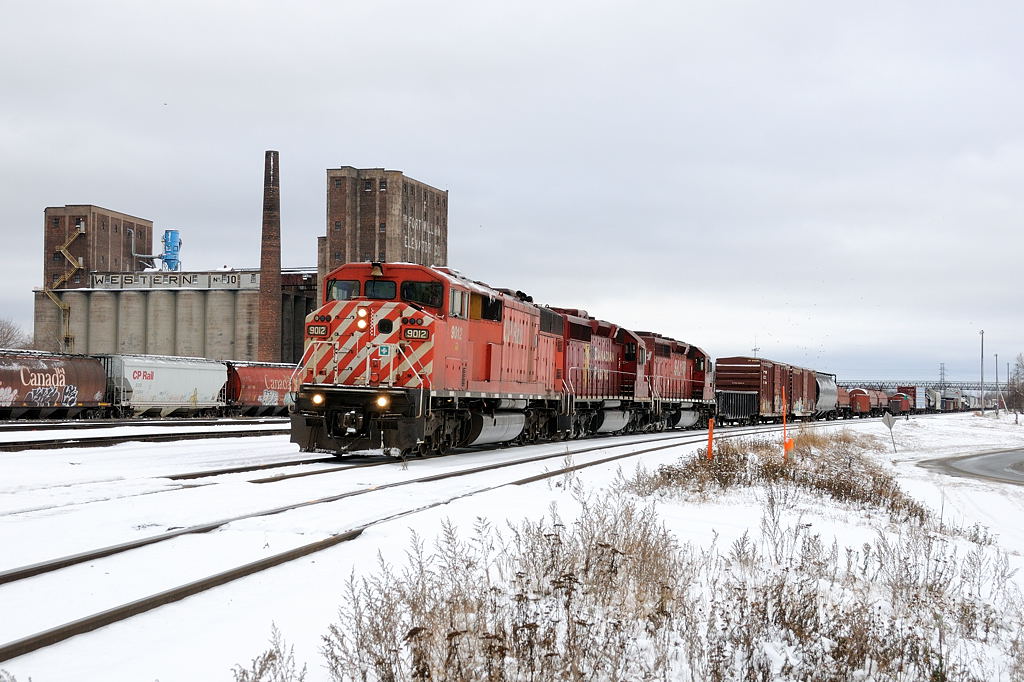 CP 9012 East, 420-26 has finally been given the okay into the terminal after holding clear at the airport for more than an hour. Initially the crew was to pull down through the yard (in the background) and cut of their tailend portion, but due to heavy congestion with a yard crew setting a \"box\" train (local CP slang for grain empties), the box train crew looking to get onto it\'s freshly built consist, empties fresh from the \"Mission\" elevators and the \"Resolute\" (paper mill) job looking to get out to the mill, along with a few through mainline freights the crew had to wait their turn. Now with a route the crew pull down to the \"Bottom end of C-yard\" to make their setoff, passing Western Grain in Westfort. Power: CP SD40-2F 9012- CP SD40-2 6602- STLH SD40-2 5651.