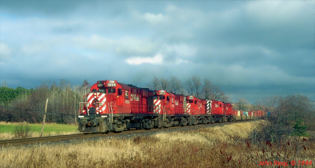 A typical 1994 all 4-axle MLW consist led by RS-18 1858 approaches Stacey Road, Hope Township with a late afternoon westbound under an ominous sky.