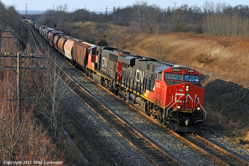 The head end of grain train 874 finds a sucker hole in the cloud cover as they climb through Lovekin. CN 2320 and 5768 lead, while 2247 and 8910 make up the mid train DPU on the 155 car, 22000 tonne train. 1432hrs.