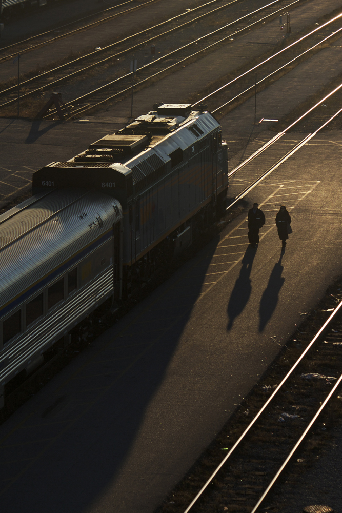 The sun is about to duck under the horizon in Mimico as two VIA Rail on-board crewmembers stroll down a service platform at VIA\'s Toronto Maintenance Centre. Either they have finished a run or they are preparing to board a train bound for points west.