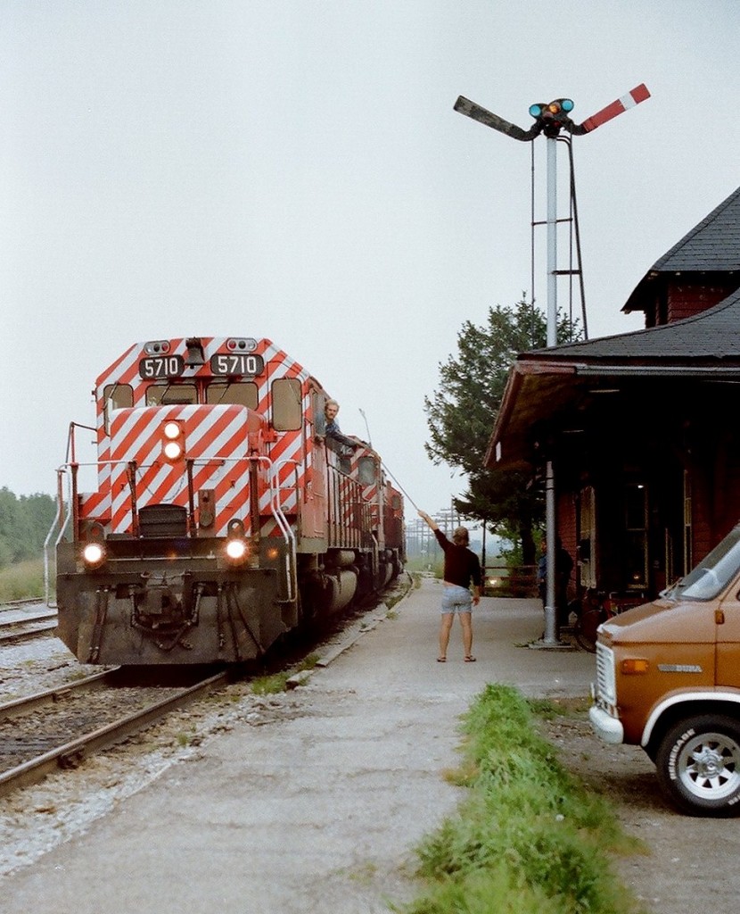 CP Rail 5710 south is hustling at track speed as the head end crew member grabs the train orders hooped by the CP Rail Bolton station operator. Love those stripes! September 1977 ASA100 Kodak colour negative. Photographer S. Danko.