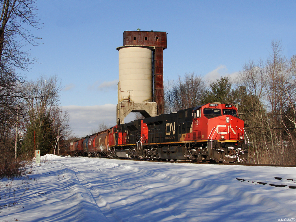 CN G87441 15 - CN 2301 South passing the old coal tower at Washago, today\'s 2+2 setup had CN 2301/8017 upfront, and CN 2101/2305 working on the tail end of 137 grain loads.