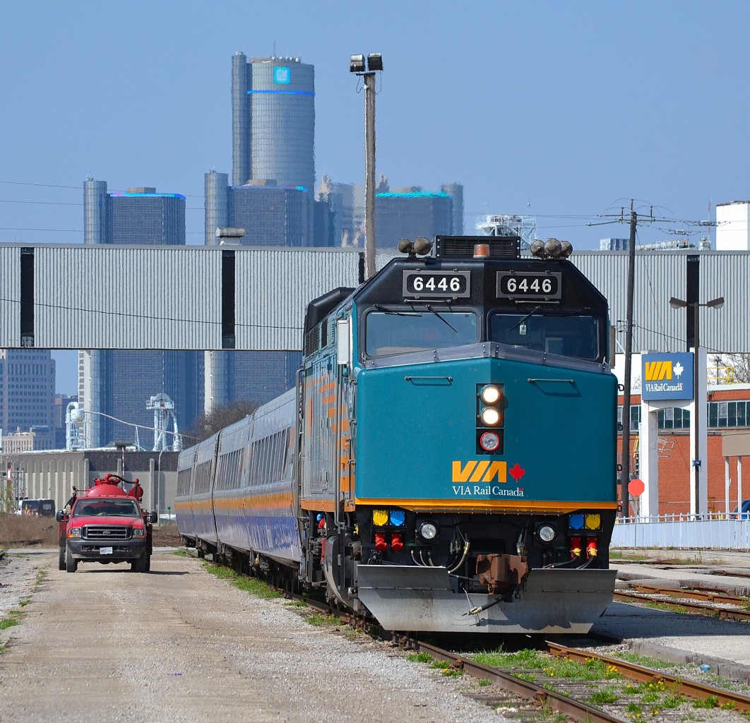 VIA 76 with 6446 sits beside the Windsor VIA station platform with the Detroit Renaissance Center in the background.