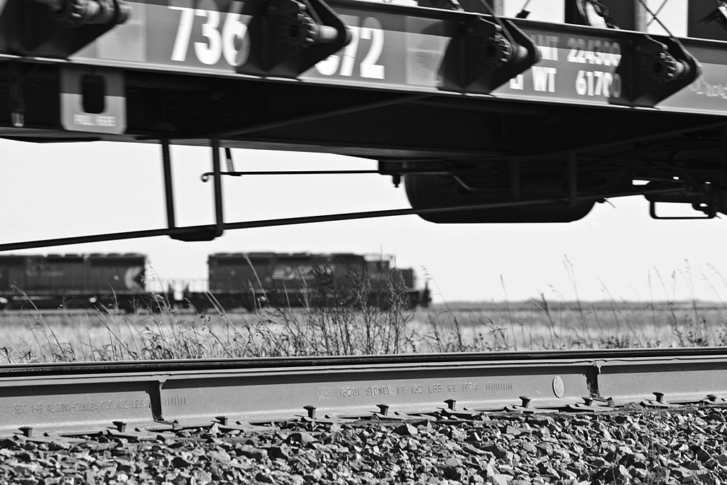 CP 6066 and 6010 wait in the distance as CN 347 rolls on by after setting of a centerbeam. CP will the get the green to work K1 Mosaic Potash mine at Cutarm.