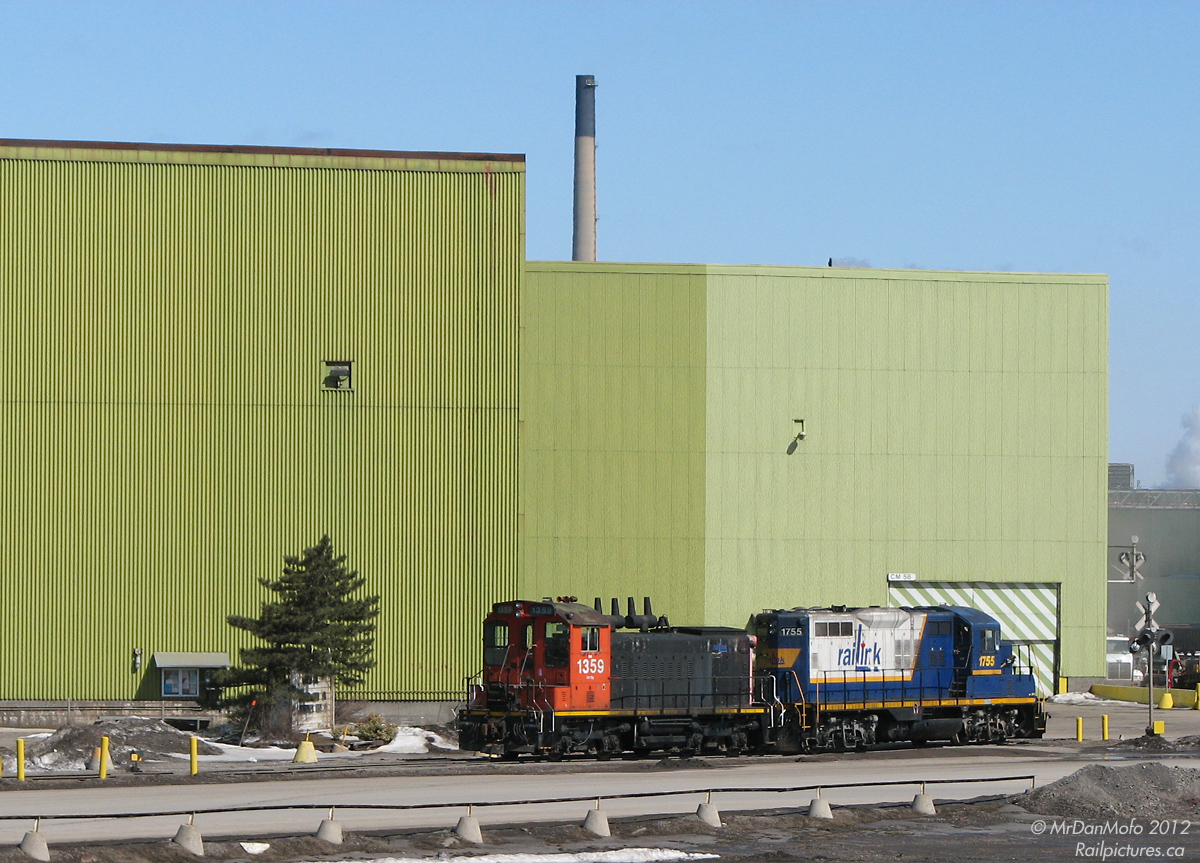 Waiting to get into US Steel\'s yard, Southern Ontario Railway 1359 (a recently reactivated ex-CN SW1200RS) and RLK GP10 1755 sit amid the gritty industrial green buildings of the former Stelco plant.