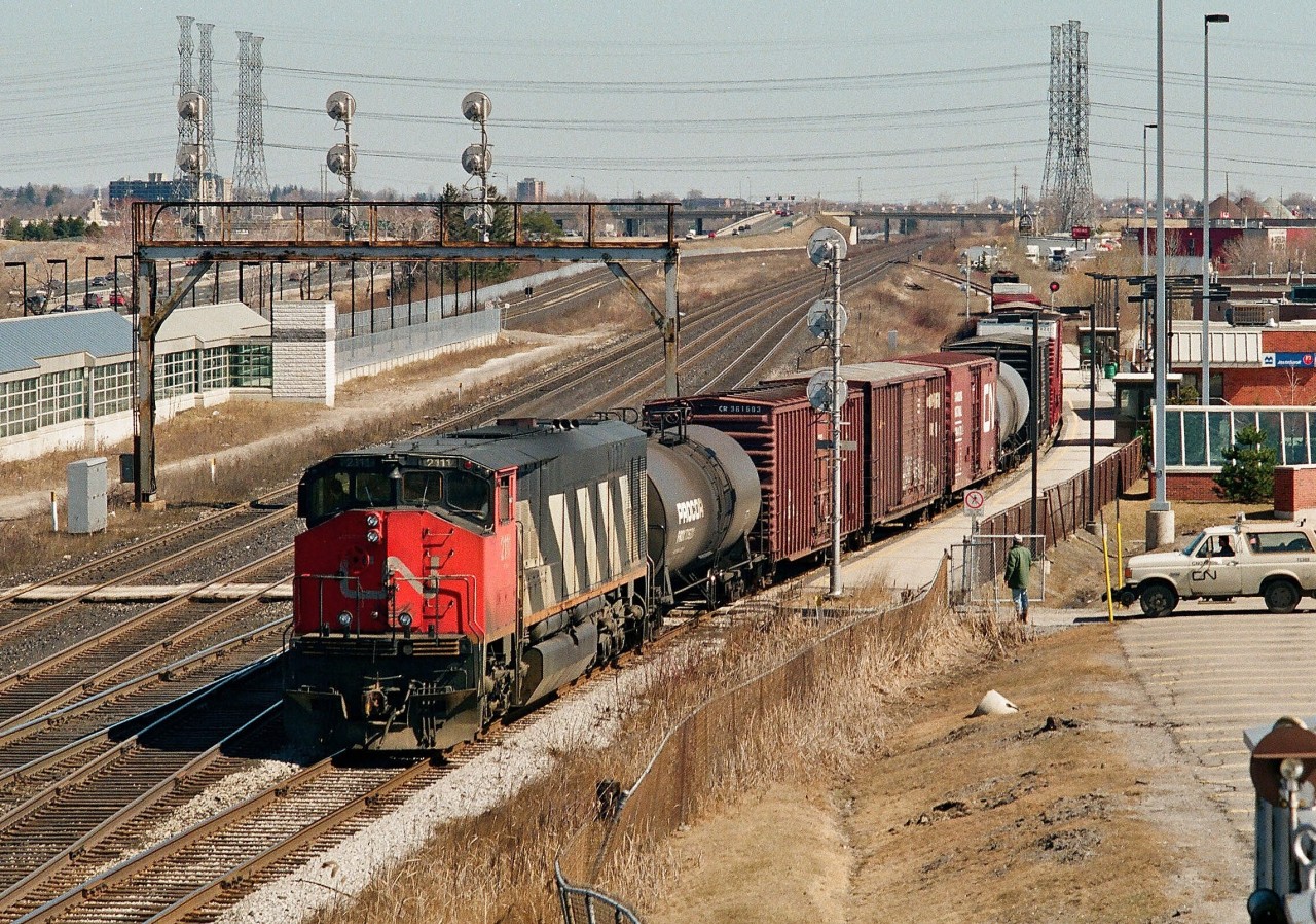 Rust Buster! 12:30 p.m. March 26, 1995, CN Kingston Subdivision mile 313.0,  Pickering, Ontario: the first train in nine days enters the Pickering GO station south platform track. This \'rust buster\' train (all empties) is crewed by management personnel and powered at the east end by CN SD40u 6016 (remanufactured 1995 by AMF, original number 5026 (GMD 1967)) and at the west end by BBD HR616 2111. The purpose of the rust buster trains (this one operated over all CN switches and tracks at Liverpool and Pickering Jct. And similarly at the GO Junction switches) is  to remove rail rust built up over the nine day national rail  stoppage in anticipation of the back to work order by the Canadian Government. Understand similar trains operated at other locations across the country (pix out there anyone?). At the same time this train operated the Canadian Parliament is conducting a Sunday session and debating the merits  of the proposed Bill C 77 to end the nine day national rail strike. Bill C 77 passed later in the day March 26, 1995 and received Royal Acent same day. ( At the time the CNR was a Crown Corporation, later in this year the CNR will become a public corporation and CN stock will commence trading on public stock exchanges). Kodak Kodacolor II negative. Photographer S. Danko.