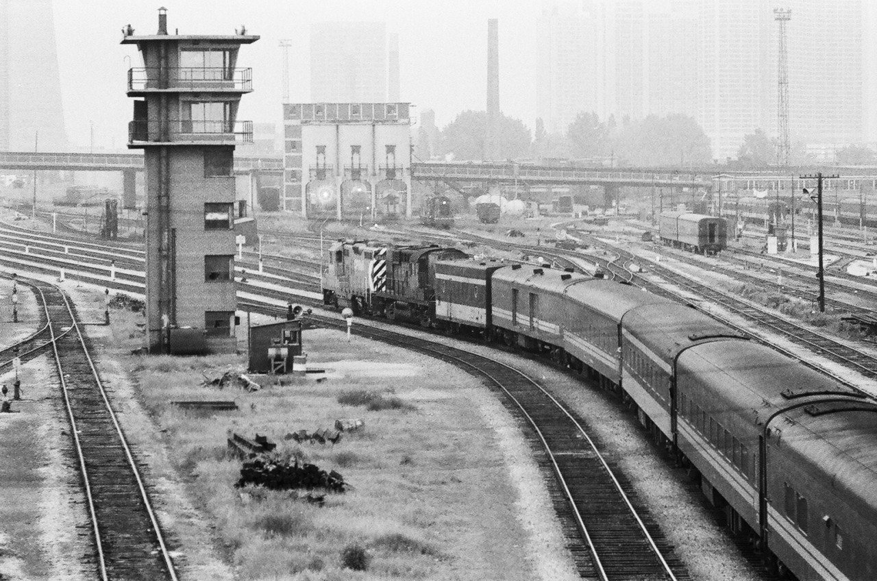 The changing eastward view from Bathurst Street: One of four images showing the changes through years: 1979, 1980\'s and 2011. Note the nearly empty Spadina coach yard (due to Sunday peak travel period) and the four main depot approach tracks curving around the never used (to my knowledge) control tower. This \'trailing shot\' image shows Train #4 (or perhaps one of the last train #2?) on Father\'s Day June 17, 1979, powered by CP Rail 8529 – 8473 (credit to Bill Millar); a GP9 – RS10 pulling an ex CN consist. The train is the \'Super Continental\' consist operating in the Via \'Canadian\' time slot. (anyone with further knowledge?). June 17 is the date of the new Via schedule that moved the Via \'Canadian\' (trains #1 and #2) to a Montreal only origination and the Via \'Super Continental\' (trains #3 and #4) to a Toronto only origination. The final westbound Via Canadian equipped with the ex CP Budd equipment departed Union June 16, 1979 – per Paul Cordingley. The time of this negative exposure is  approximately 8:30 p.m., the available light was very poor and add to that this is Kodak TriX 400 ASA pan film – hence please excuse the low contrast and somewhat grainy exposure (the later the train is the longer you wait!). It would be some six plus years  before Toronto would be the terminal for the ex CPR Budd (\'The Canadian\') equipment again. Special thanks for viewers input on the approach photo (and circumstances surrounding this image): Bill Millar, Paul Cordingley).  Kodak Tri X Pan b&w negative film. Photographer S. Danko