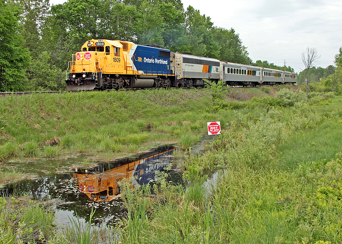 Who needs sunshine when you\'ve got sqeaky-clean 1809 to brighten the scene? The swamp is quickly drying up due to an unusually dry spring but there\'s still enough standing water to catch a reflection of this shiny beast as it passes the Mile 138 marker on the CN Newmarket Sub.