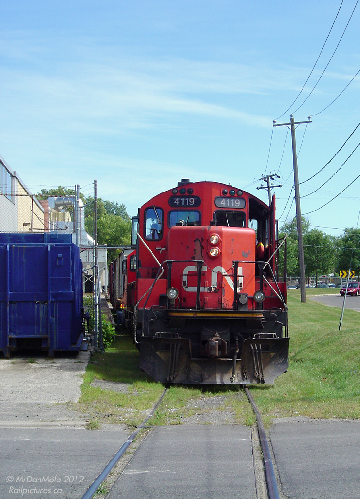 In the west side of Brampton, far away from the industrial areas around Bramalea and Hwy 410, two CN GP9RM\'s pause south of Nelson Street as crewmembers couple onto a string of boxcars at the Georgia Pacific plant. Built in 1949, the factory at Queen & McMurchy was originally home to the Dixie Cup Company (once sporting a giant Dixie Cup on the roof) and as of 2006, was the last customer in downtown Brampton to use rail service. About a year or two later, the switch to the weed-infested Dixie Cup Spur was removed during triple-tracking for the Georgetown GO expansion and was never reinstalled: after almost 60 years, the last rail customer in downtown Brampton switched to trucks.