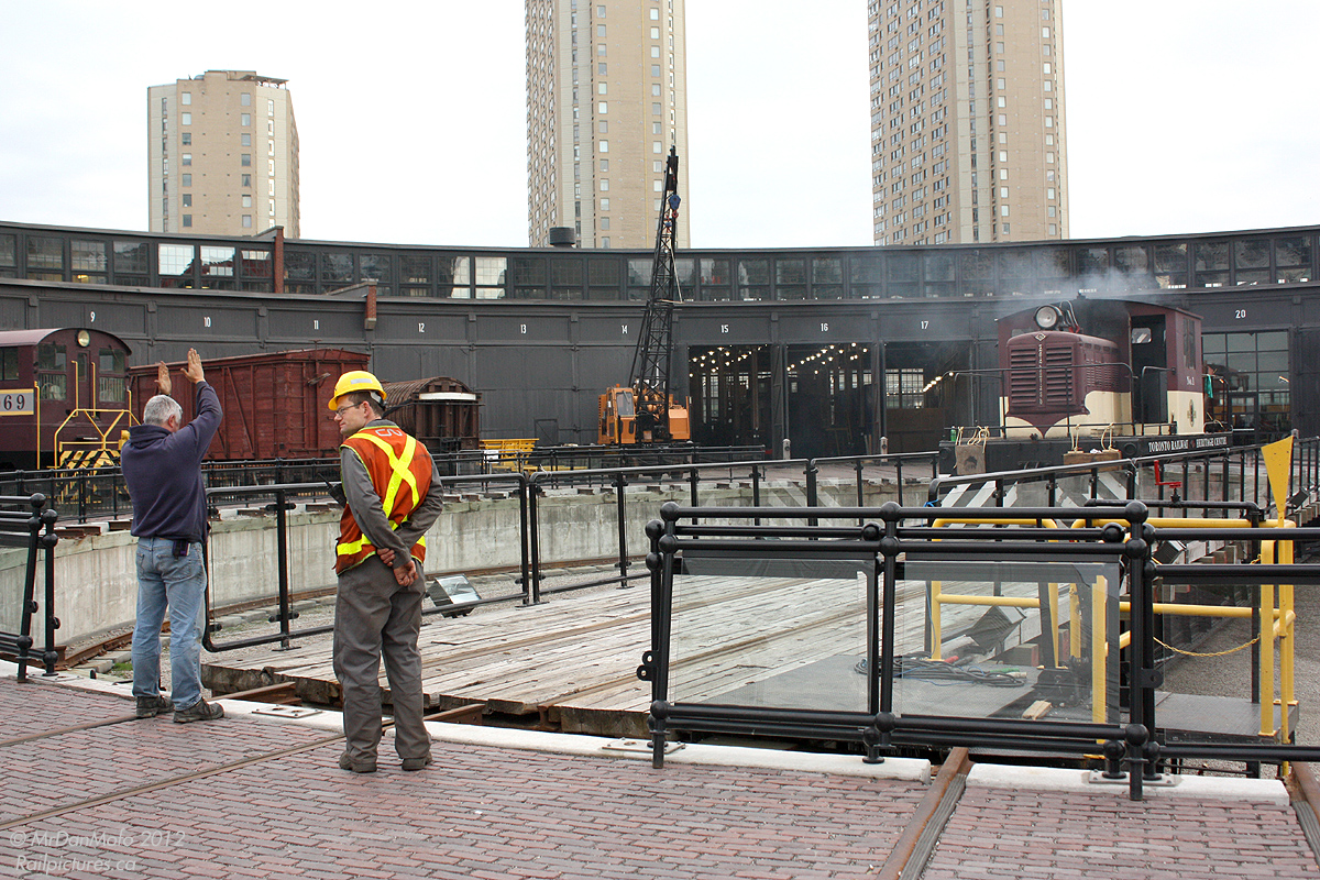 One of the challenges in railroading for as long as there were roundhouses: aligning the turntable properly. Museum volunteers at the Toronto Railway Heritage Association\'s Roundhouse Park make some final alignment adjustments before their little CLC-Whitcomb switcher goes to couple onto a British steam engine, in town for \"The Railway Children\" production in Toronto.