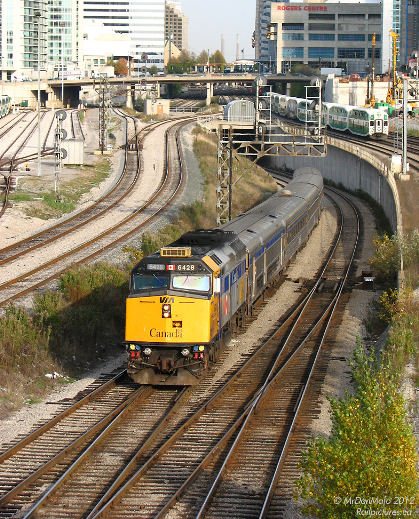 After having departed Toronto\'s Union Station minutes before, VIA F40PH 6428 gets train #75 under way, coming out from under the flyunder at Bathurst Street and onto the Oakville Sub. In the backgound, GO trains are making their way to Union Station to take on evening loads of commuters leaving the city for the suburbs.