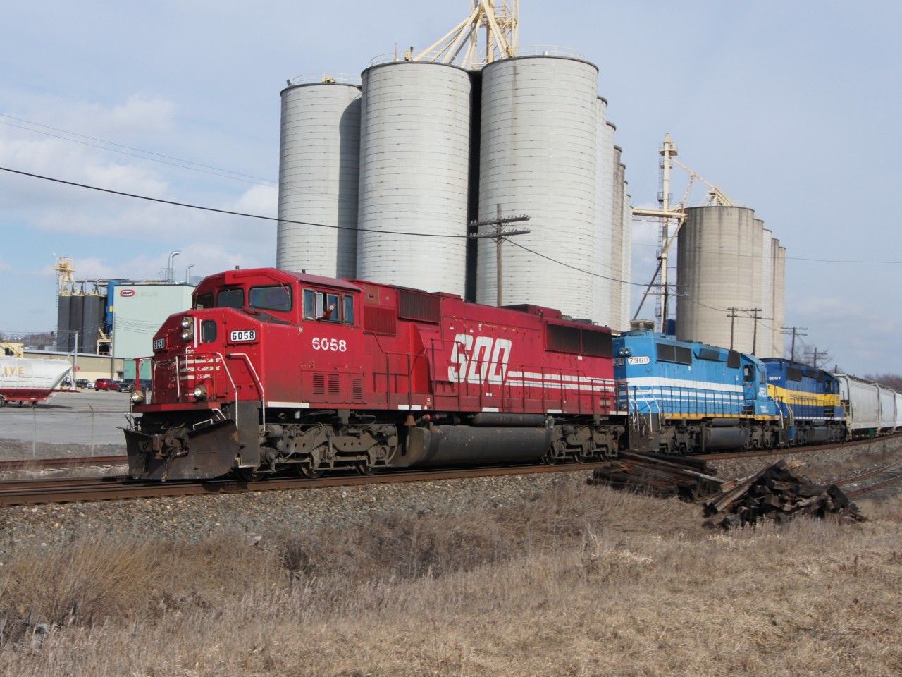 With a wave from the conductor, SOO 6058 leads NREX 7360 and DME 6097 westbound past ADM Milling. Having just crossed the Credit River, the train would soon pass through Streetsville GO Station and by the yard at Streetsville Junction.