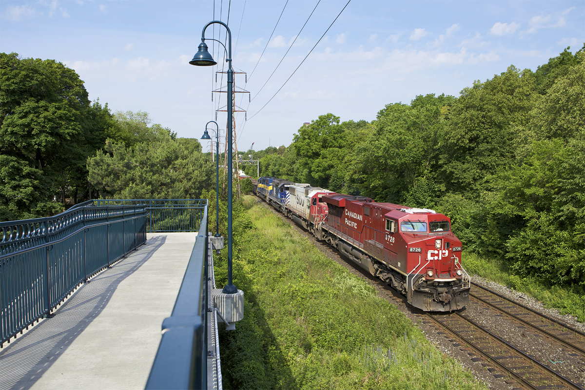 On a humid June morning, CP 8726, along with SOO 6024, ICE 6102 (ex-IMRL), and ICE 6416 "City of Linwood" lead a moderately sized eastbound past MacLennan pedestrian bridge.