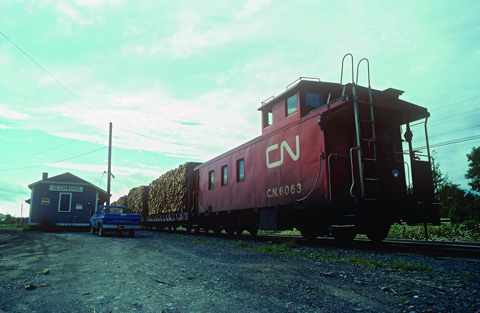 [Editors note: Despite the color issue, the image is accepted for rarity - none of this exists today and is all abandoned]  The Lewisporte switcher is making up its train of pulpwood at Glenwood. The loading area was just west of the depot on a spur. After the train is complete, it will depart for Bishop's Falls.