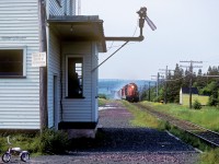 Remarks: Train 204, the mainline freight from Port-aux-Basques (ferry terminal and yard on the southwest coast) to St. John's, approaches Goobies in a cloud of brake shoe smoke (there were no dynamic brakes in Newfoundland). Note the agent looking out the window at the arriving train. Goobies was on CN's St. John's Subdivision, 20.9 miles east of Clarenville.