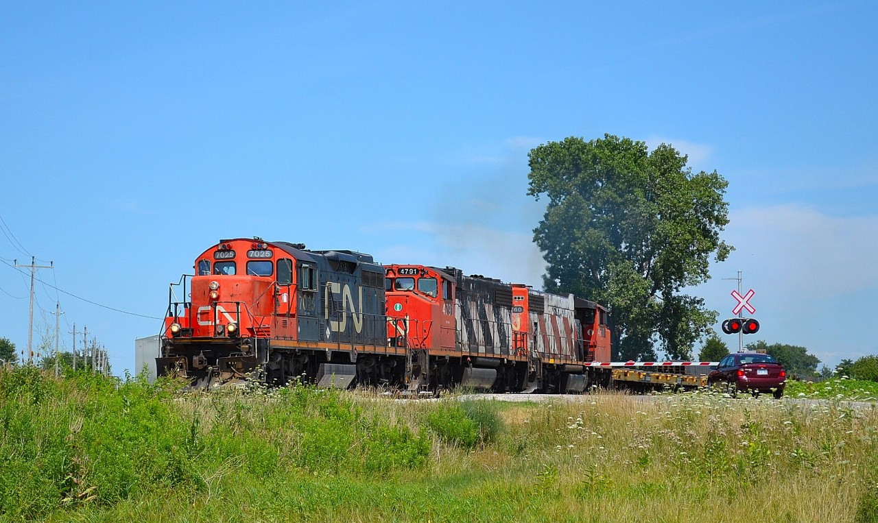 CN 439 with the local power 7025 added up front for extra power, chugs westbound past the Hwy#2 crossing as it approaches the Ringold Diamond with an extra long load consisting of multiple cars of I-beams.