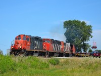 CN 439 with the local power 7025 added up front for extra power, chugs westbound past the Hwy#2 crossing as it approaches the Ringold Diamond with an extra long load consisting of multiple cars of I-beams.