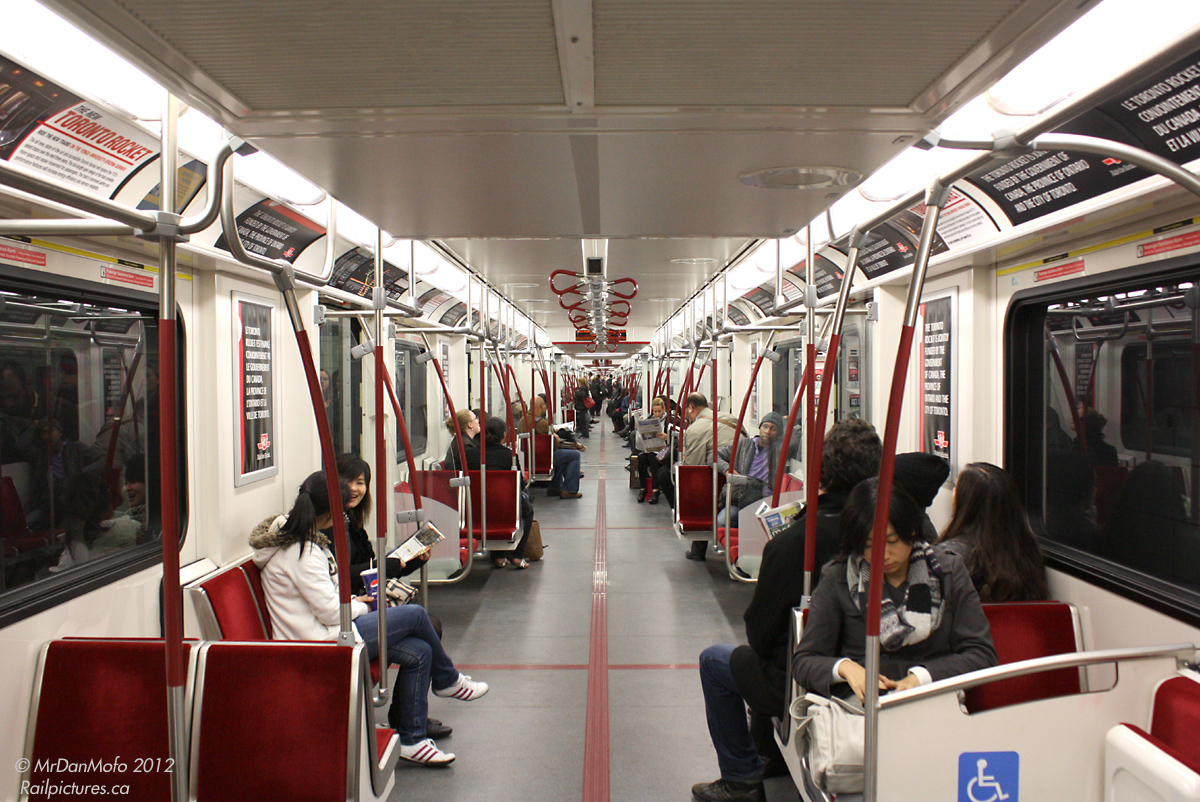 Interior of a brand-new TTC "Toronto Rocket" subway car, built by Bombardier in Thunder Bay. The entire train is semi-permanently coupled, with open walkways at the ends of each car to increase passenger capacity allow movement inside the train. The photographer is looking from the end car 5411, through 5412, 5413, etc to the other end car at the opposite end of the train, 5416. Also, the photographer doesn't recommend running from end to end while the train is in motion.