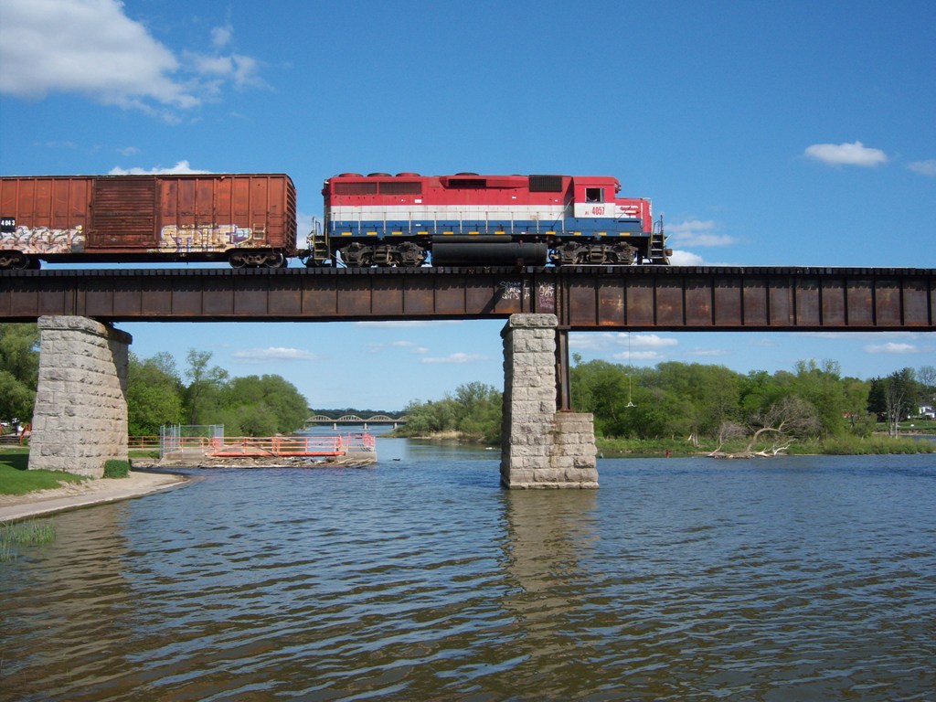 RLK 4057 is pulling eleven cars across the Grand River at Caledonia.  At this point they are about a third of a way across the bridge.  With the impending sale of Rail America, in the next few years we may see a photo of an Orange and Black GP40-2 crossing the bridge.