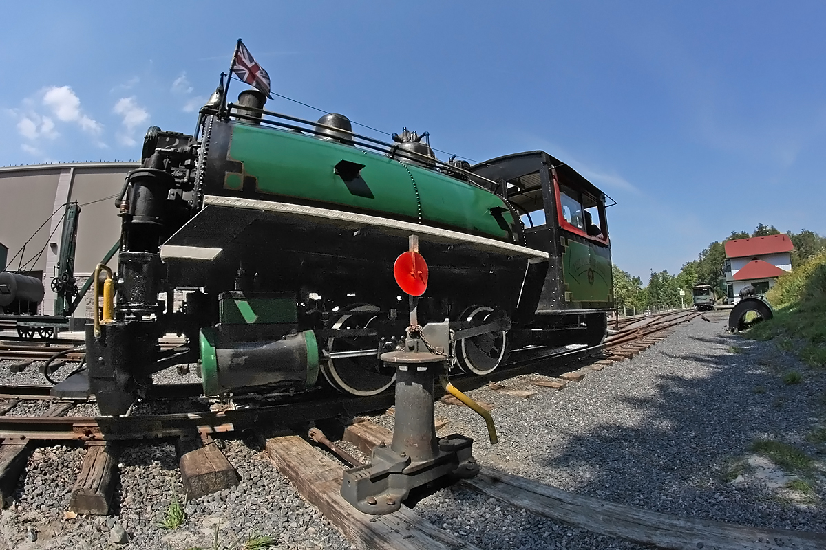 Number 2 eases over the switch points for the crossover from Track 1 to Track 2 after uncoupling from its train - which is visible by the Rotary Village Station in the background - on its way to the turntable to be spun around. Then it will run around the coahes and hook up to wait for the next run. Also visible in this shot are the saddle tank for Number 1 sitting forlornly in the grass on the right hand side waiting for the day it will once again be mounted over the boiler and filled with water to make its own runs up and down the line. Number 1 has a couple of cracks in the boiler that need to be repaired before it can be steamed up, and also is in need of an air puimp (under construction at present) and conversion from coal to oil-firing for safety and economic reasons among others. We're hoping to get her at least close to completion next year, if given the go-ahead by the town.